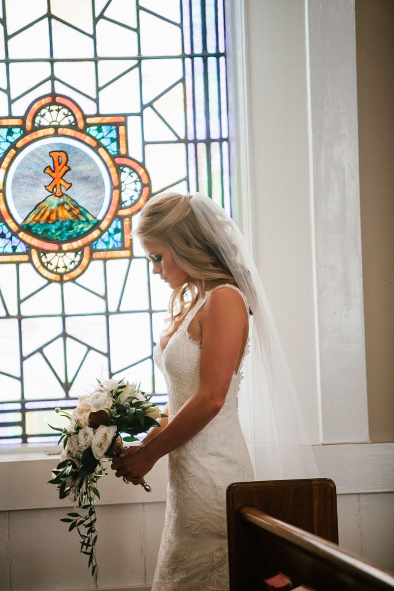 Bride praying in front of stain glass window with bouquet in hand